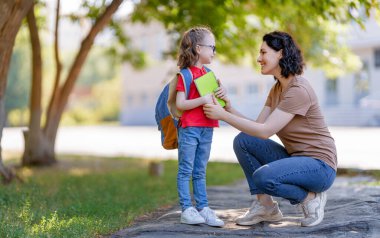 İlkokulun ebeveynleri ve öğrencileri el ele gider. Sırt çantalı kadın ve kız. Dersler başlıyor. Sonbaharın ilk günü.