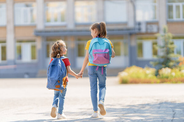 Pupils of primary school. Girls with backpacks outdoors. Beginning of lessons. First day of fall.    