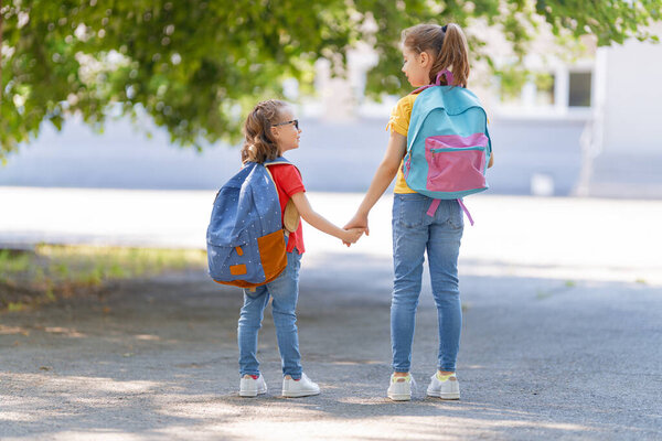 Pupils of primary school. Girls with backpacks outdoors. Beginning of lessons. First day of fall.    