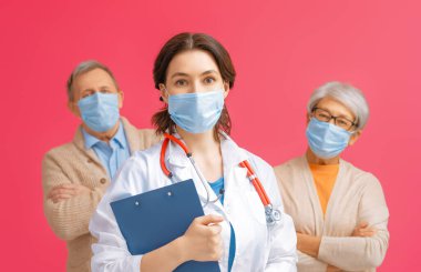 Doktor ve yaşlı çift koronavirüs ve grip salgını sırasında maske takıyor. Virüs koruması, ev karantinası. COVID-2019. Maske takıyor. Kırmızı pembe arka plandaki insanlar.