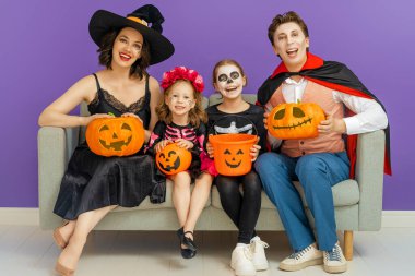 Anne, baba ve çocukları partide eğleniyorlar. Cadılar Bayramı 'nı kutlayan mutlu aile. İnsanlar mor arka planda karnaval kostümü ve makyaj giyiyorlar..