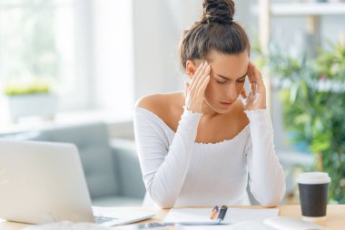 İnternette okuyan genç bir iş kadını, Webinar izliyor, dizüstü bilgisayarda podcast yapıyor ve başı ağrıyor. E-öğrenme kavramı.