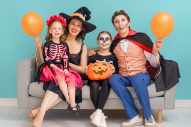 Anne, baba ve çocukları partide eğleniyorlar. Cadılar Bayramı 'nı kutlayan mutlu aile. Gökyüzü duvarında karnaval kostümü ve makyaj giyen insanlar..