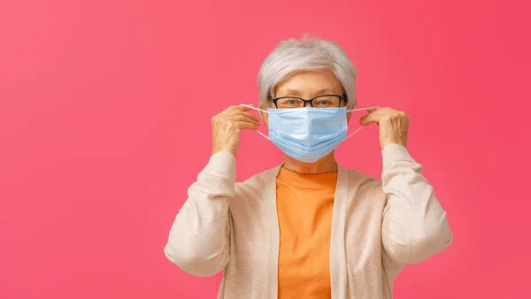 在大肠病毒和流感爆发时戴着面罩的老年妇女 病毒和疾病防护 家庭隔离 Covid 2019 戴上或摘下面具 红色背景的人 — 图库照片
