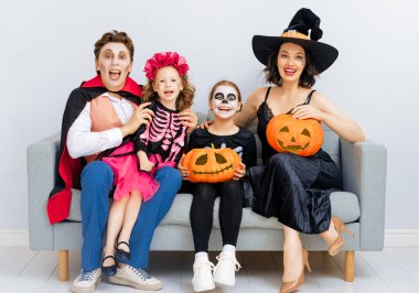Anne, baba ve çocukları partide eğleniyorlar. Cadılar Bayramı 'nı kutlayan mutlu aile. Beyaz duvar arkasında karnaval kostümü ve makyaj giyen insanlar..