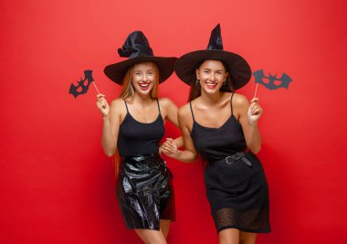 Mutlu Cadılar Bayramı! Siyah cadı kostümlü iki genç kadın kırmızı arka planda partide..