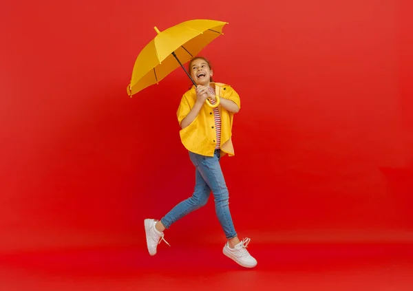 幸せな感情的な子供の笑いとジャンプ 赤い背景に黄色の傘を持つ子供 — ストック写真