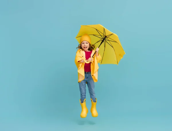 Happy emotional child laughing and jumping. Kid with yellow umbrella on colored teal background.