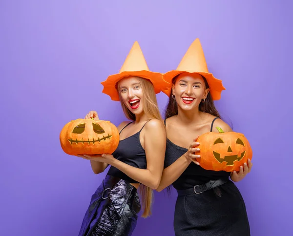 万圣节快乐 两个穿着黑色女巫服装的年轻女人 穿着紫色背景的南瓜派对服 — 图库照片