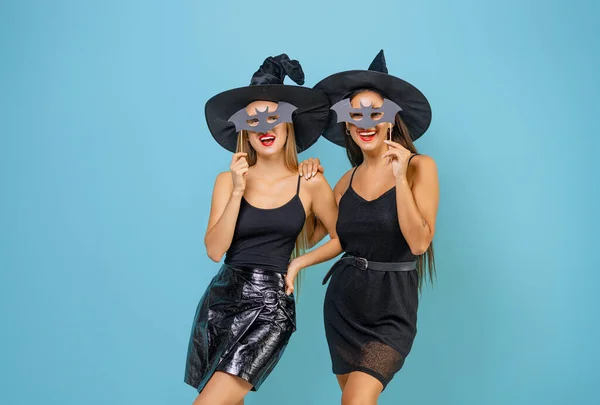 Happy Halloween! Two young women in black witch costumes on party on teal color background.