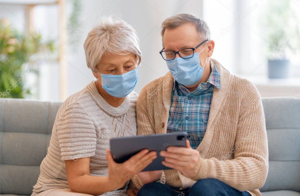 Senior couple wearing facemasks and using tablet pc during coronavirus and flu outbreak. Virus and illness protection, home quarantine. COVID-2019. Taking on or taking off masks.