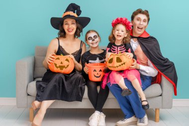 Anne, baba ve çocukları partide eğleniyorlar. Cadılar Bayramı 'nı kutlayan mutlu aile. Gökyüzü duvarında karnaval kostümü ve makyaj giyen insanlar..