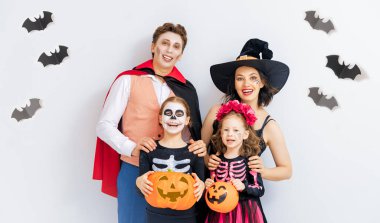 Anne, baba ve çocukları partide eğleniyorlar. Cadılar Bayramı 'nı kutlayan mutlu aile. Beyaz duvar arkasında karnaval kostümü ve makyaj giyen insanlar..