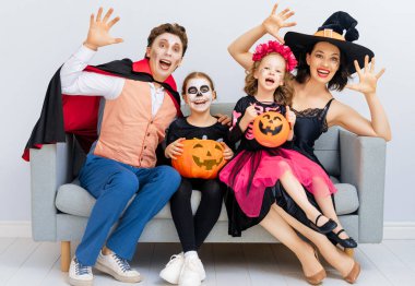 Anne, baba ve çocukları partide eğleniyorlar. Cadılar Bayramı 'nı kutlayan mutlu aile. Beyaz duvar arkasında karnaval kostümü ve makyaj giyen insanlar..