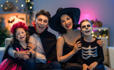 Anne, baba ve çocukları evde eğleniyorlar. Cadılar Bayramı 'nı kutlayan mutlu aile. İnsanlar karnaval kostümü ve makyaj yapıyor..