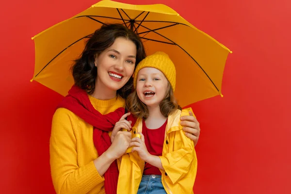 喜怒无常的孩子和她的母亲笑着拥抱 带黄色雨伞的家庭 红色背景 — 图库照片