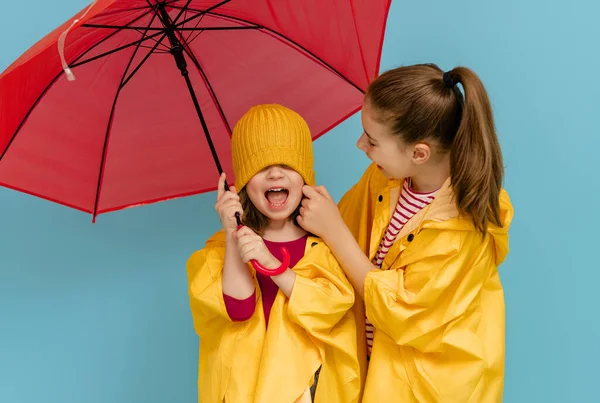 Happy emotional children laughing and embracing. Kids with red umbrella on colored teal background.