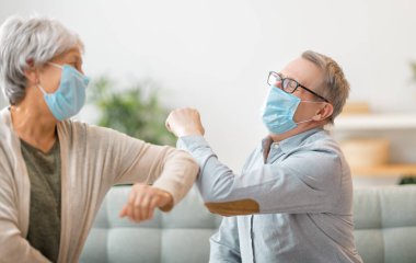 Kıdemli çift yüz maskesi takıyor ve Coronavirus ve grip salgını sırasında dirseklerini çarpıştırıyor. Virüs ve hastalık koruması, ev karantinası. COVID-2019.