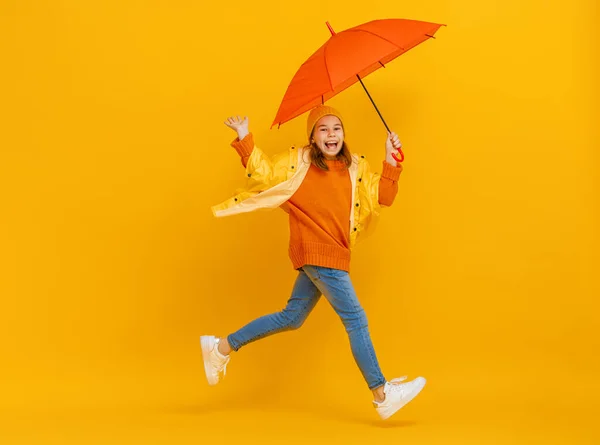 快乐的情绪孩子又笑又跳 红色背景上挂着橙色雨伞的孩子 — 图库照片