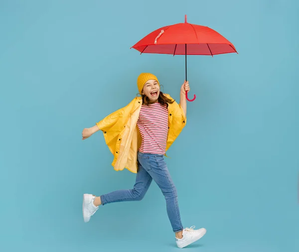 Happy emotional child laughing and jumping. Kid with red umbrella on colored teal background.