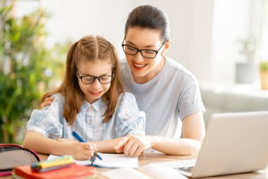 Okula dönelim. Mutlu çocuk ve yetişkin masada oturuyor. Ödev yapan ya da online eğitim alan kız.