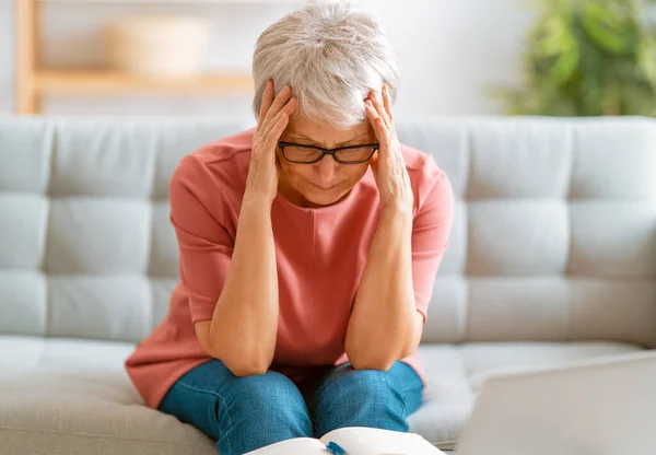 坐在家里沙发上头疼的年迈疲惫的女人 — 图库照片