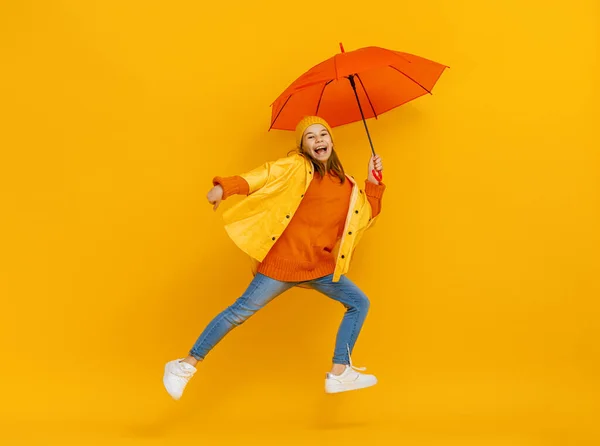 快乐的情绪孩子又笑又跳 红色背景上挂着橙色雨伞的孩子 — 图库照片