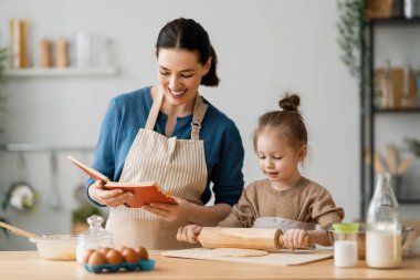 Mutlu aile birlikte fırın hazırlıyor. Anne ve kız çocuk kurabiye pişiriyor ve mutfakta eğleniyorlar. Ev yapımı yemek ve küçük bir yardımcı.. 