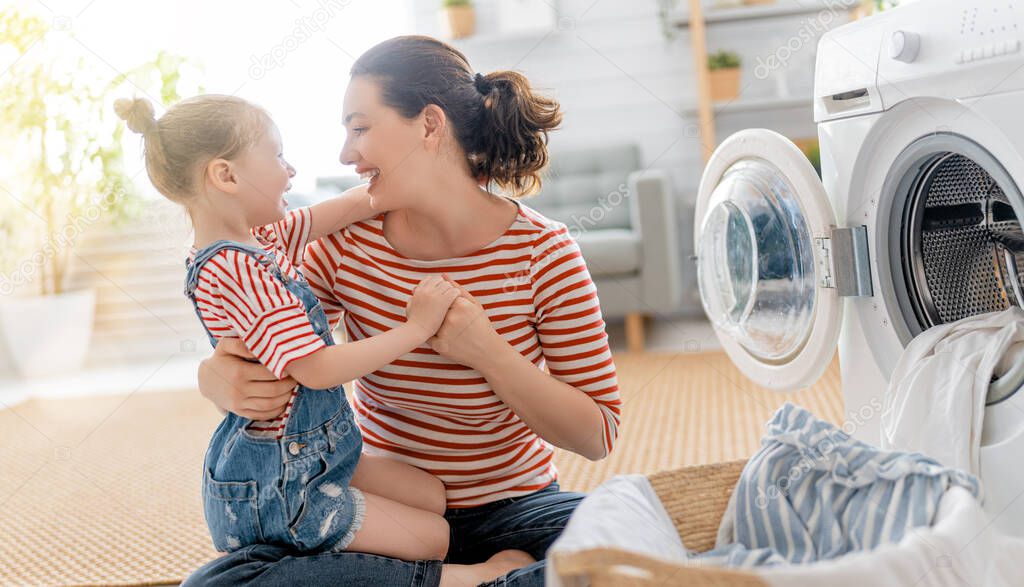 Beautiful young woman and child girl little helper are having fun and smiling while doing laundry at home.