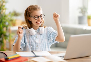 Okula dönelim. Mutlu çocuk masada oturuyor. Ödev yapan ya da online eğitim alan kız.