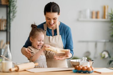 Mutlu aile birlikte fırın hazırlıyor. Anne ve kız çocuk kurabiye pişiriyor ve mutfakta eğleniyorlar. Ev yapımı yemek ve küçük bir yardımcı..  