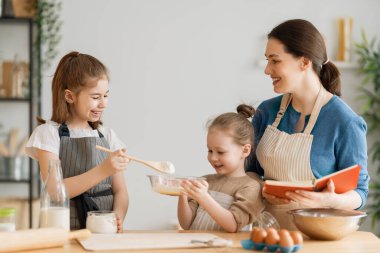 Mutlu aile birlikte fırın hazırlıyor. Anne ve çocuk kızları kurabiye pişiriyor ve mutfakta eğleniyorlar. Ev yapımı yemek ve küçük bir yardımcı.. 