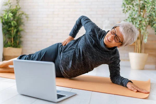 Aktif Giyimde Kıdemli Bir Kadın Evde Egzersiz Yaparken Dizüstü Bilgisayarda — Stok fotoğraf