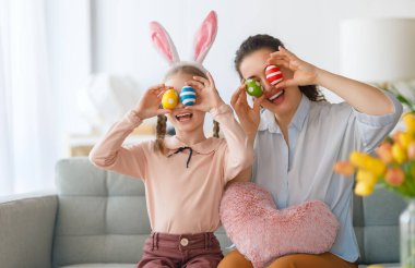 İyi tatiller! Anne ve kızı yumurta boyuyor. Paskalyayı kutlayan aile. Sevimli küçük kız tavşan kulağı takıyor..