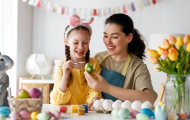 Anne ve kızı yumurta boyuyor. Mutlu aile Paskalya için hazırlanıyor. Tavşan kulağı takan şirin bir kız çocuğu..