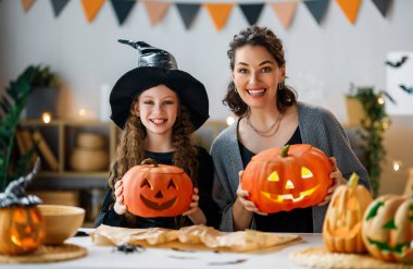 Mutlu aile Cadılar Bayramı için hazırlanıyor. Anne ve çocuk evde balkabağı oyuyor..