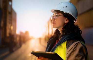 Beyaz şapkalı kadın endüstriyel mühendis konteyner terminalinde çalışıyor..