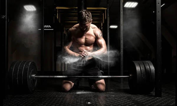 Muscular man clapping hands and preparing for workout at a gym. Focus on dust