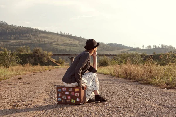 Women with vintage travel suitcase at old road