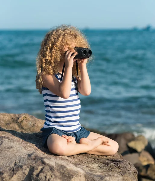 海の近くの岩の上に座って 双眼鏡を使って遠くを見て少女 — ストック写真