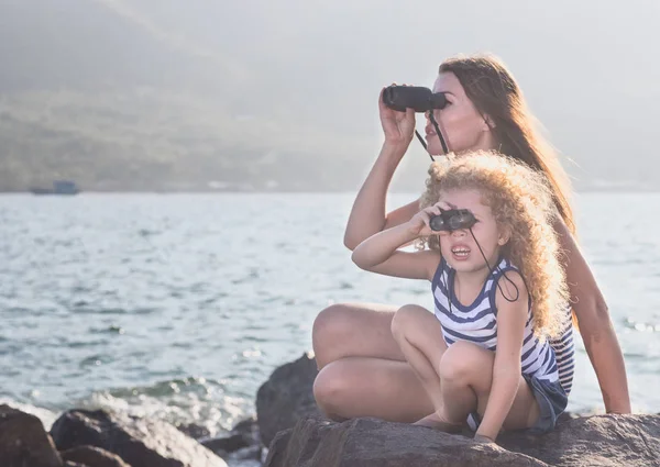 小さな女の子と母岩の上に座って 双眼鏡を使って遠くを見て近くの海 — ストック写真