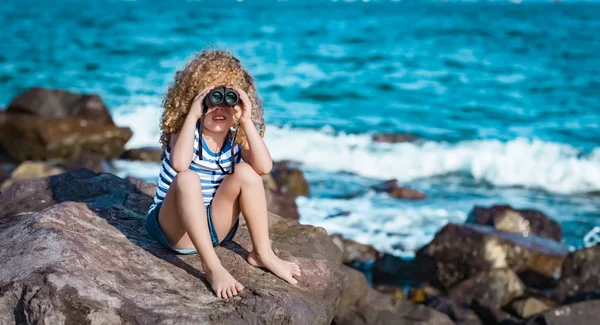 海の近くの岩の上に座って 双眼鏡を使って遠くを見て少女 — ストック写真