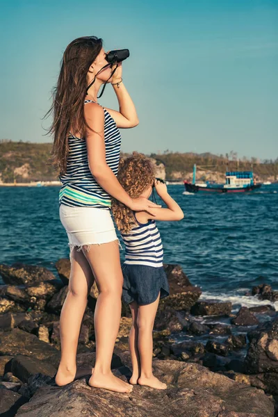 小さな女の子と母岩の上に座って 双眼鏡を使って遠くを見て近くの海 — ストック写真