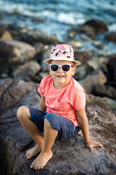 Küçük Boy Gülümseyerek Bir Deniz Kenarında Kayanın Üzerine Oturuyor — Stok fotoğraf