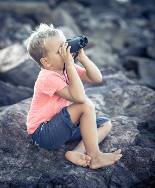 海の近くの岩の上に座って 双眼鏡を使って遠くを見て少年 — ストック写真