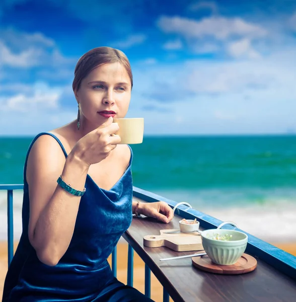 Όμορφη γυναίκα που απολαμβάνει τσάι στο καφέ βεράντα στη θάλασσα — Φωτογραφία Αρχείου