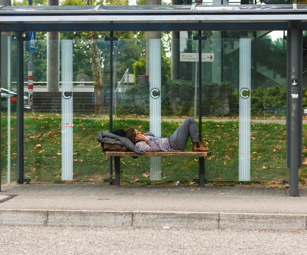 A man lies on a bench in the street