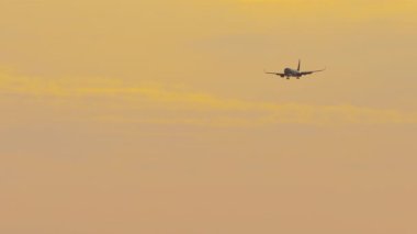 İniş takımlarını indirmiş yolcu jeti, altın bir günbatımı gökyüzüne iniş için yaklaşıyor. Düşük bir ihtimal. Uçak seyahati, turizm ve uçuş promosyonu için ideal.