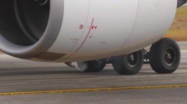 Jet motorunun detaylı görüntüsü ve önlüğe park edilmiş ticari bir uçağın iniş takımları. Seyahat, yer tutma ve modern havacılık teknolojisi.