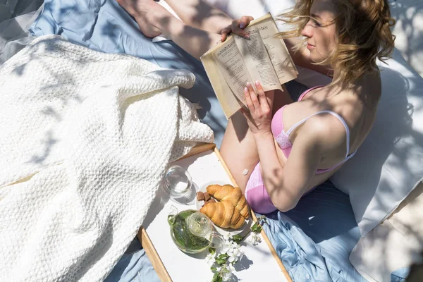 Nő az ágyban, a kertben könyvet olvasva — Stock Fotó